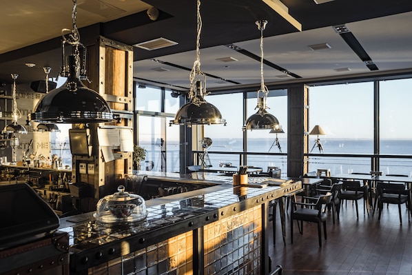 Un espace bar moderne avec vue sur l’océan, agrémenté de luminaires suspendus, d’un poêle et d’un comptoir.