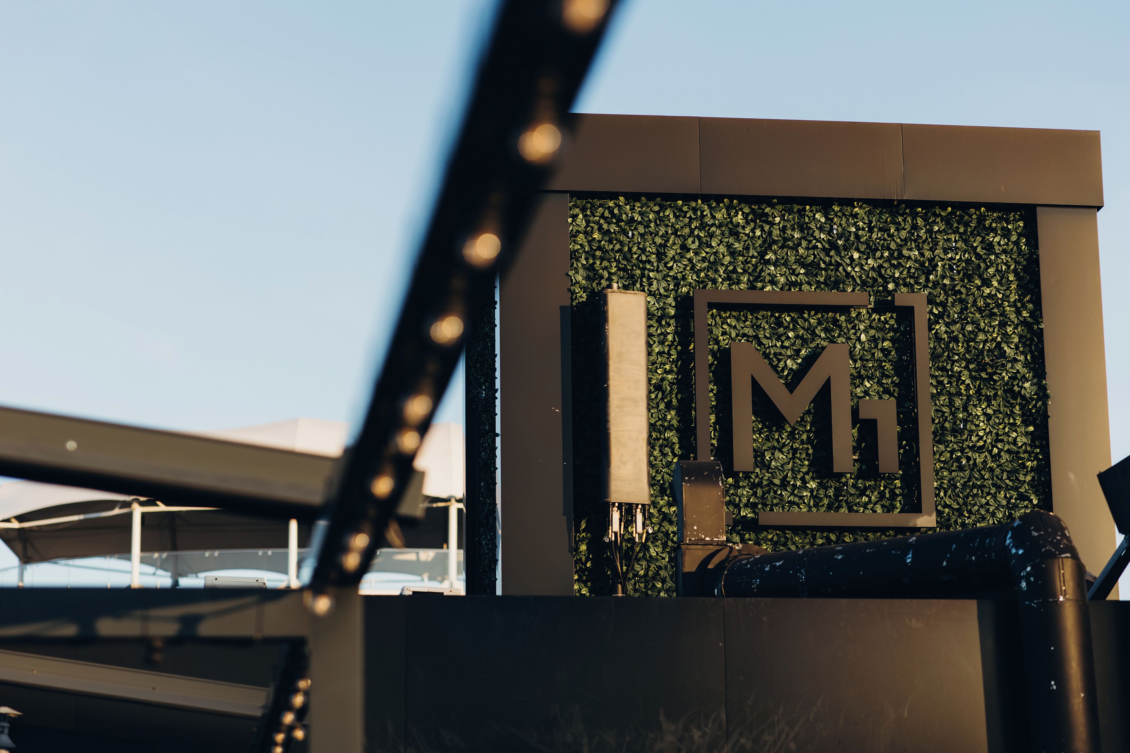 Une façade d’immeuble ornée d’un grand logo en forme de « M », d’une grille métallique et d’un mur végétal.