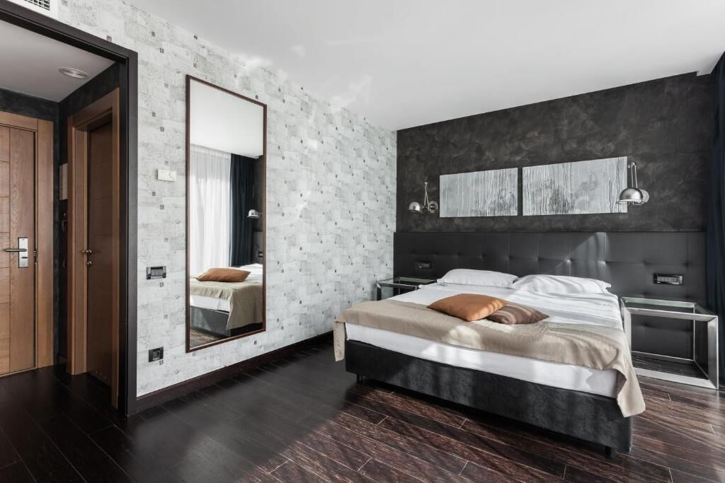 A modern bedroom with a large bed, a dark headboard, and a mirror on the wall.
