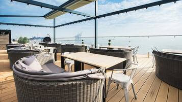 Une terrasse extérieure aménagée avec des meubles en osier, une table en bois et une vue sur l’eau.