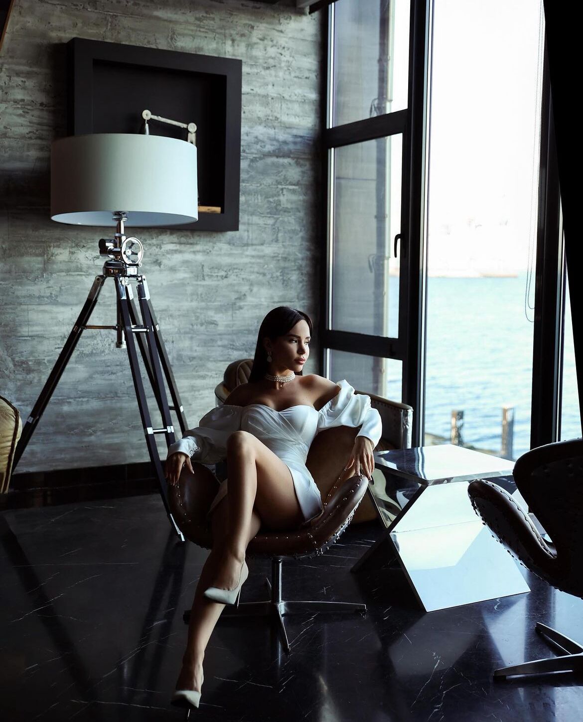 A room with a large window, a tripod lamp, and a chair.