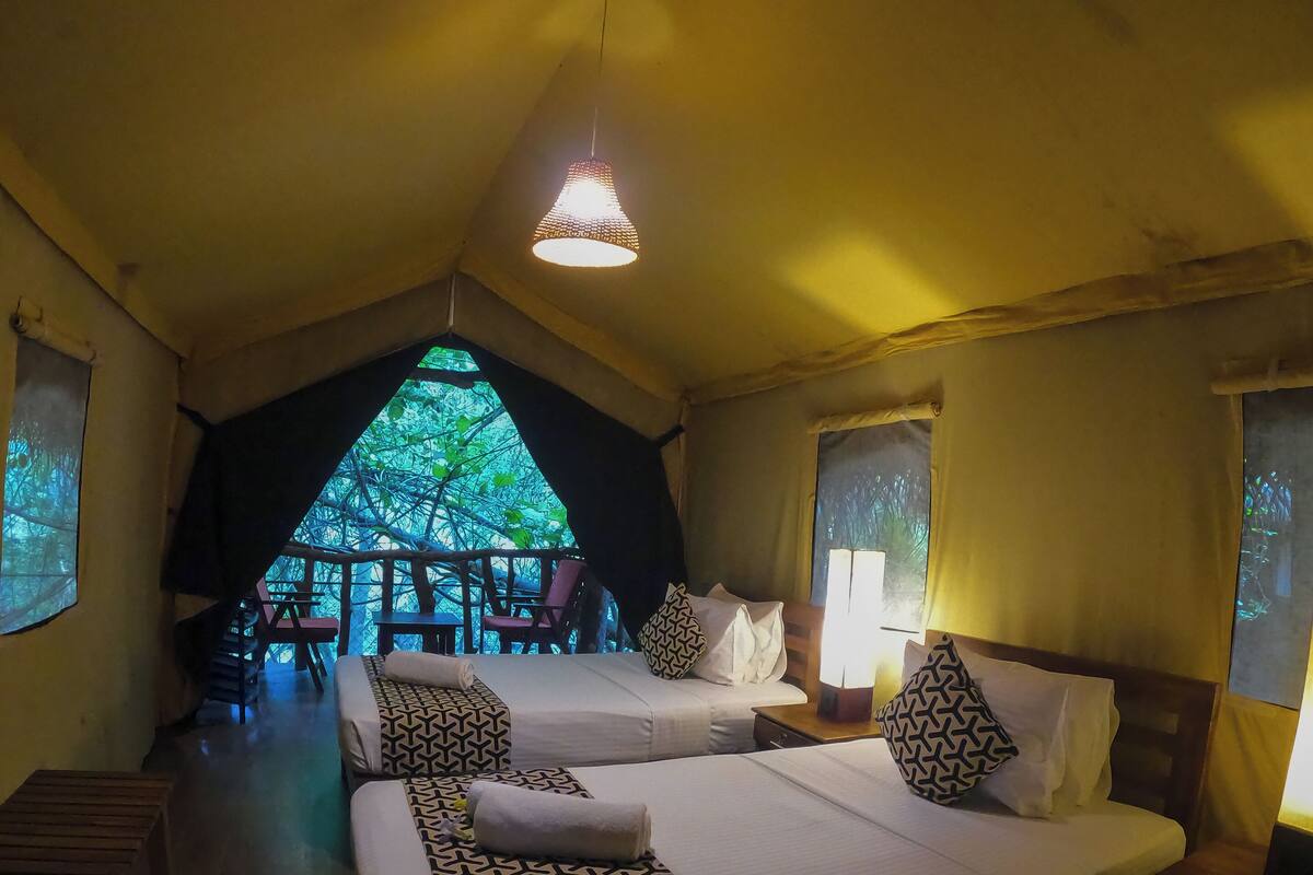 Een knus, gedempt verlichte kamer met twee bedden, een hanglamp en uitzicht op groen buiten.