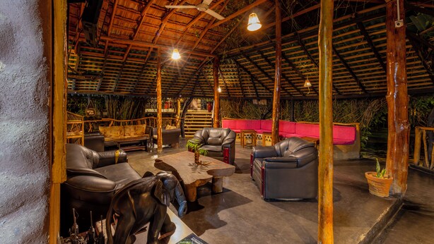 A spacious indoor area with leather sofas, a wooden coffee table, and a ceiling fan. - Athgira River Camp (Udawalawa)