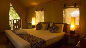 A spacious bedroom with a large bed, two bedside lamps, and a view of the outdoors. - Athgira River Camp (Udawalawa)