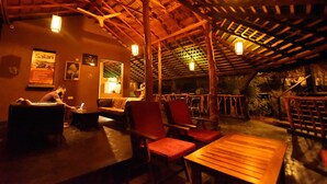 A dimly lit indoor space with wooden furniture, a ceiling fan, and a poster on the wall. - Athgira River Camp (Udawalawa)