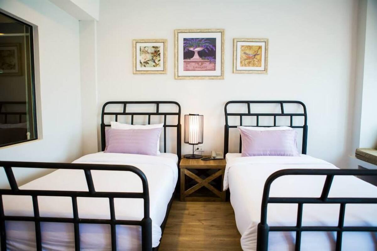 A room with two single beds, a nightstand with a lamp, and three framed pictures on the wall.