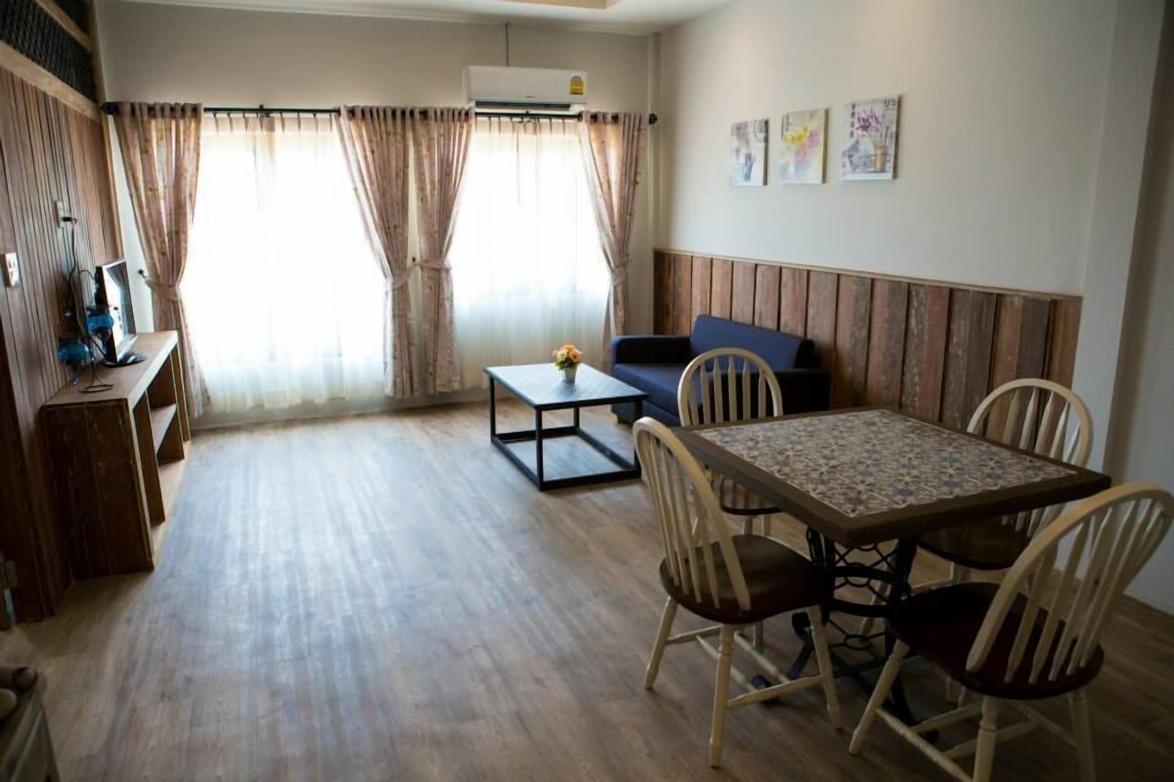A room with a wooden floor, a dining table with chairs, a sofa, and a TV on a stand.