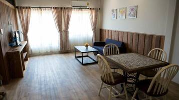 A room with a wooden floor, a dining table with chairs, a sofa, and a TV on a stand.