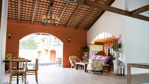 An open-plan living area with a tiled floor, wooden furniture, and a view through an archway to an outdoor space. - Hotel Toscana Trad (Trat)