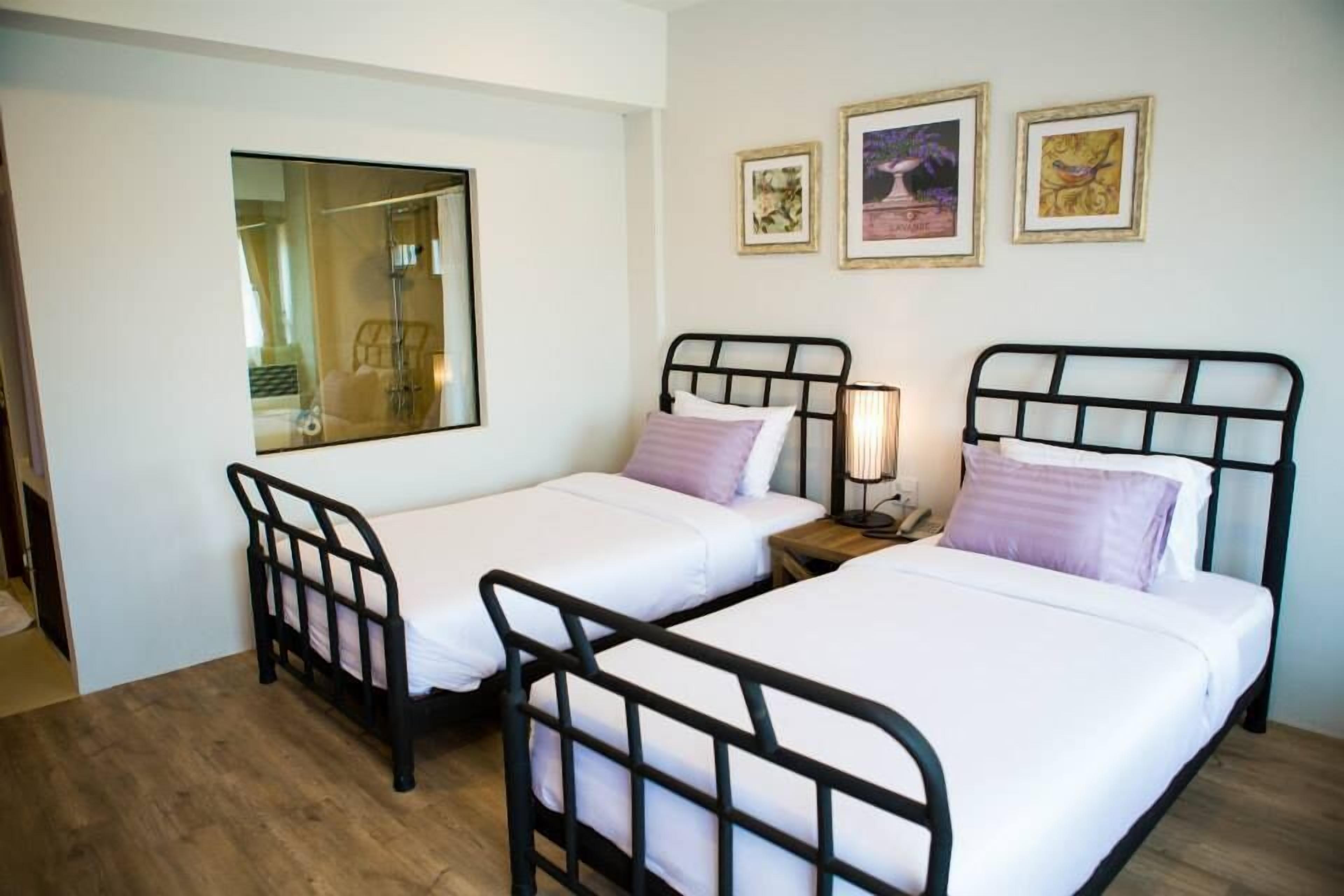 Une chambre avec deux lits simples, une table de chevet avec une lampe et un miroir au mur.