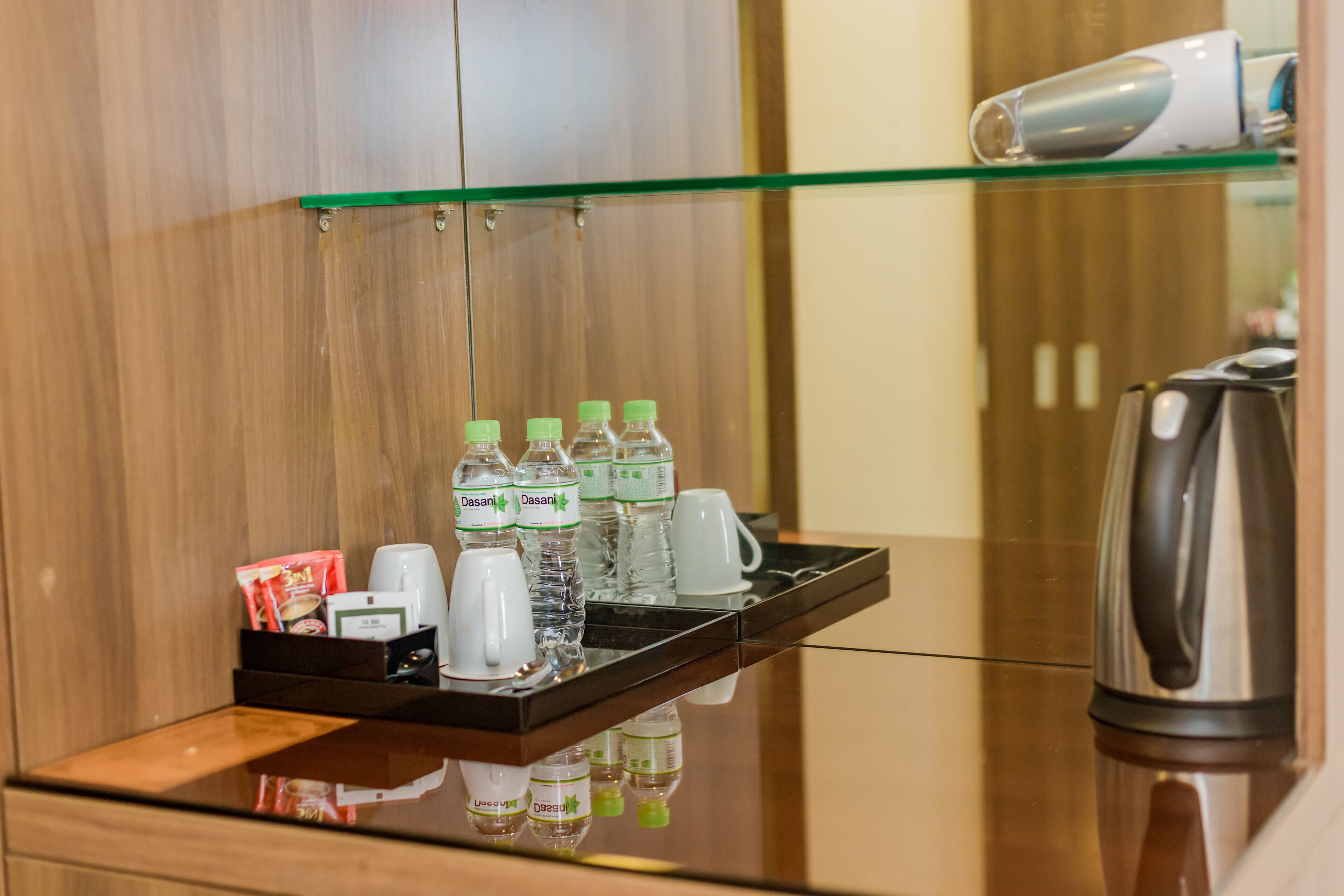 Un mini-bar d’hôtel contenant des bouteilles d’eau, des tasses à café et une bouilloire.
