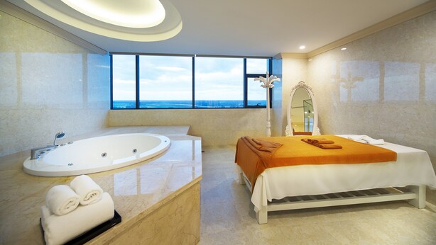 A modern bathroom with a large bathtub, a sink, and a bed with an orange blanket. - Muong Thanh Grand Quang Nam (Da Nang)