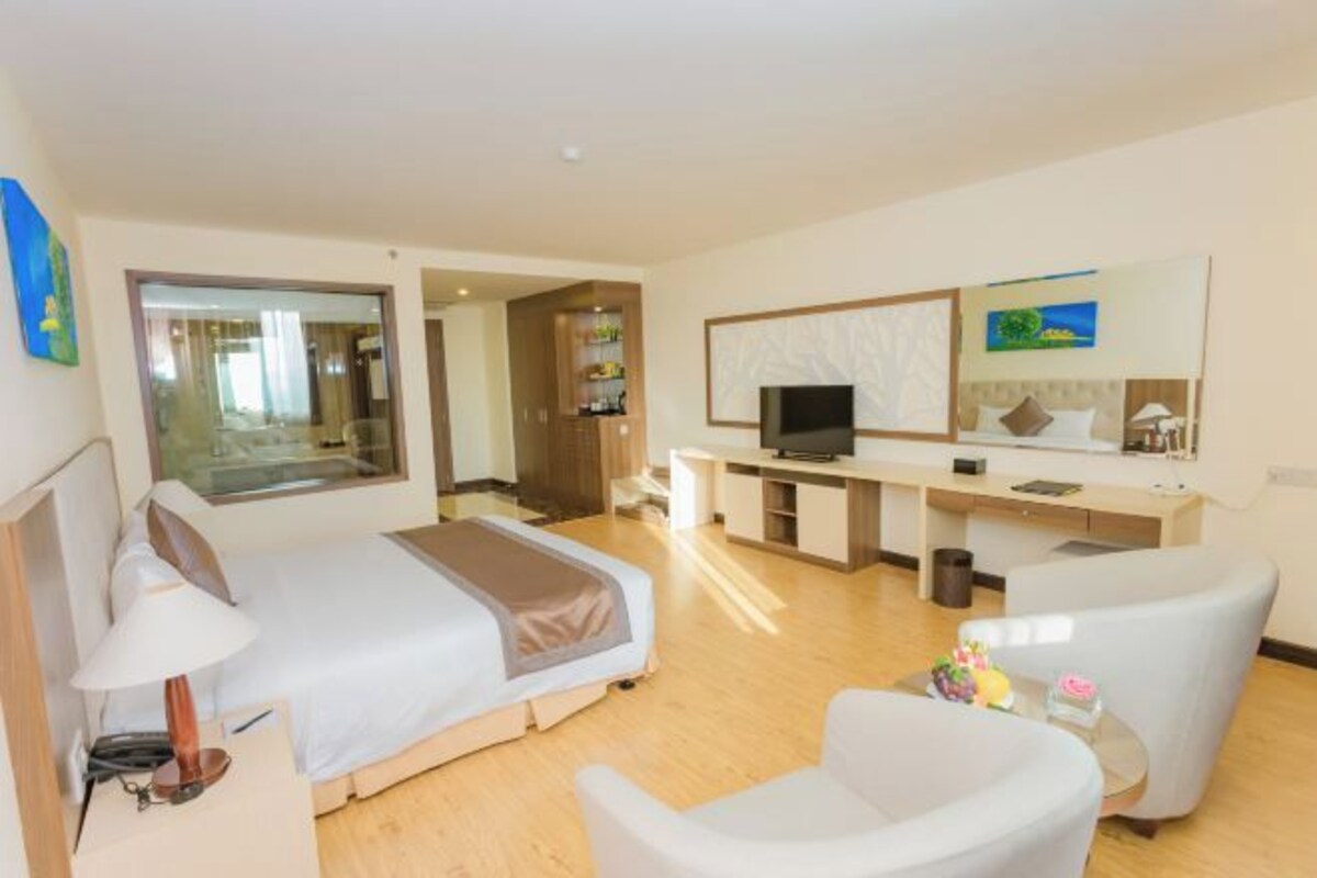 A hotel room with a bed, a desk with a TV, a chair, and a small table with items on it.