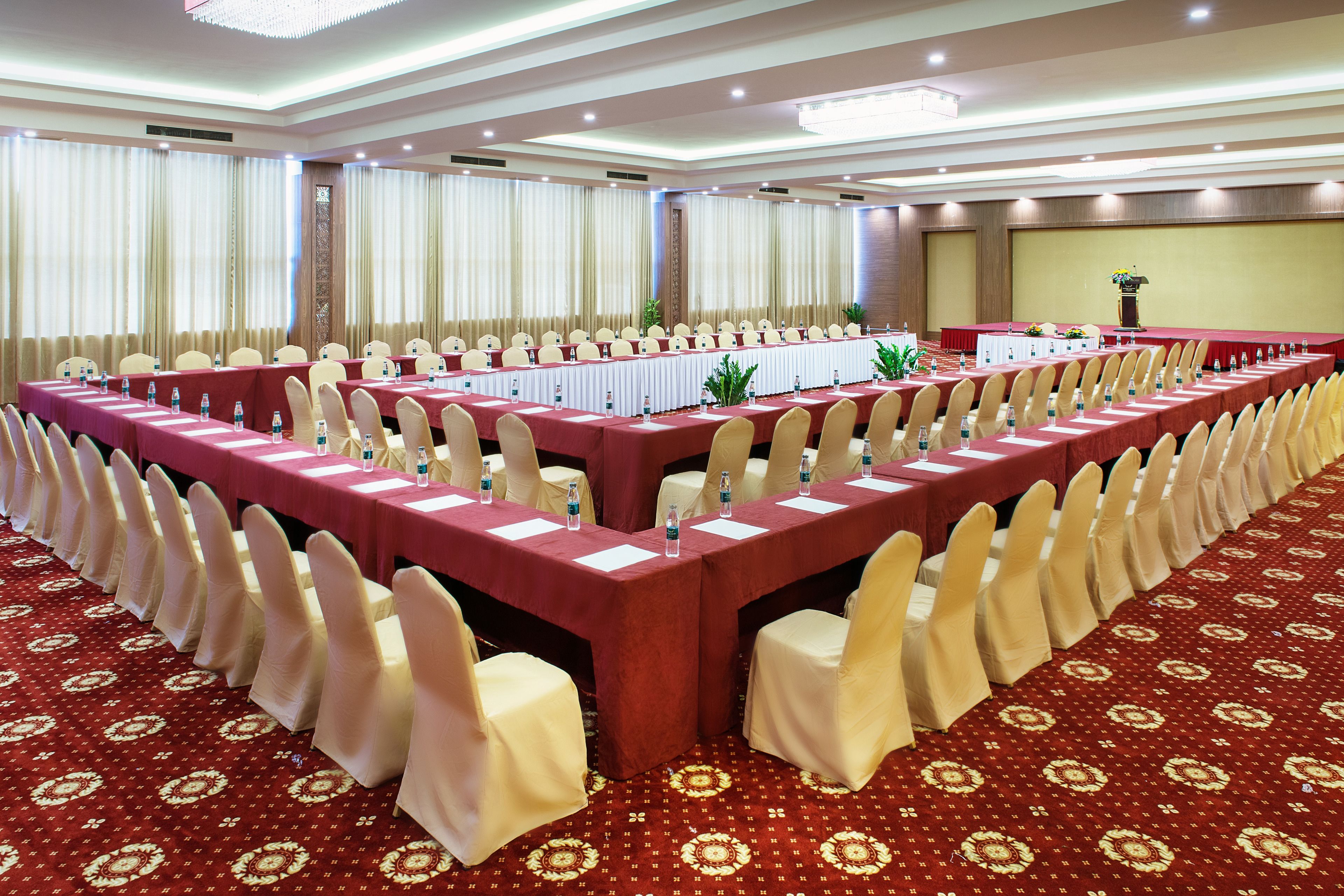 Un salón de conferencias con mesas largas, sillas y piso alfombrado.