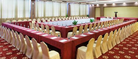 Un salón de conferencias con mesas largas, sillas y piso alfombrado.