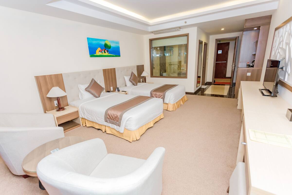 Une chambre d’hôtel avec deux lits, un bureau, une chaise, une lampe et un tableau au mur.