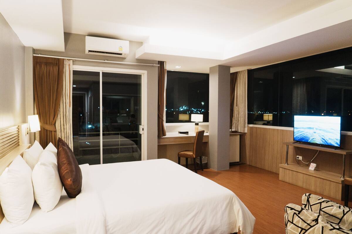A hotel room with a bed, a desk, a TV, and a view of the city at night.