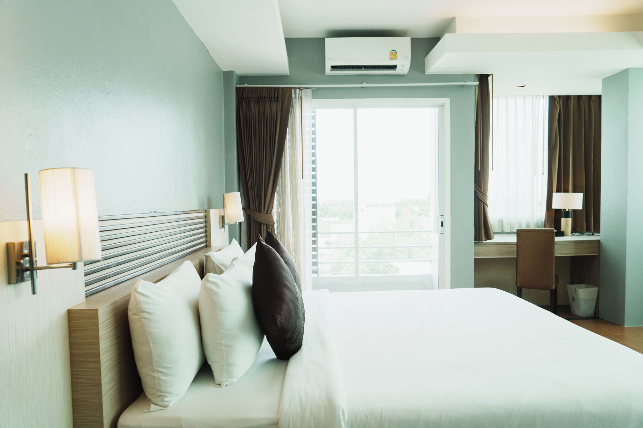 Una habitación de hotel con una cama, un escritorio, una silla, una lámpara y un equipo de aire acondicionado.