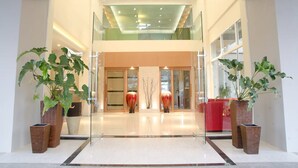 A modern hotel lobby with a glass entrance, large potted plants, and a red sofa. - Green Hotel & Resort Khon Kaen (Khon Kaen)