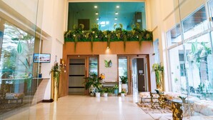 A hotel lobby with a glass wall, a reception desk, and a seating area with tables and chairs. - Green Hotel & Resort Khon Kaen (Khon Kaen)
