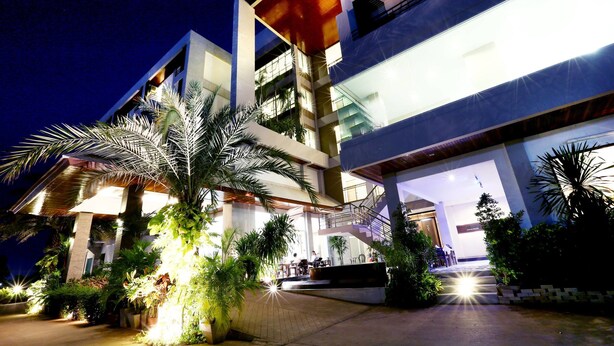 A modern multi-story building with a well-lit entrance and outdoor seating area. - Green Hotel & Resort Khon Kaen (Khon Kaen)