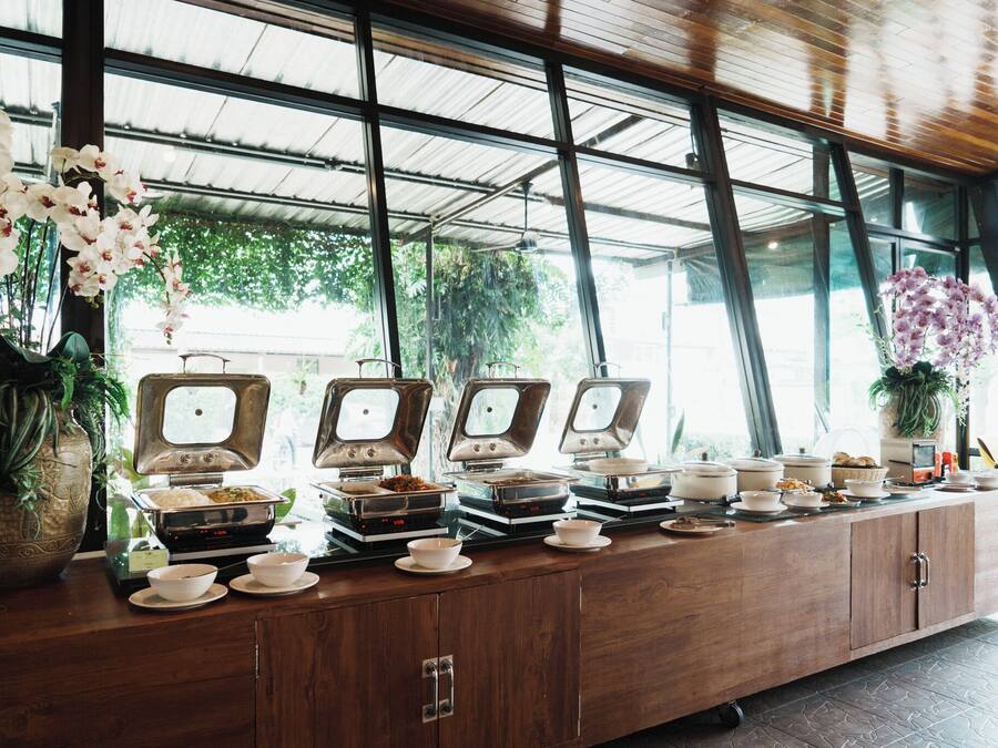 A buffet setup with multiple serving stations, a wooden cabinet, and large windows allowing natural light.
