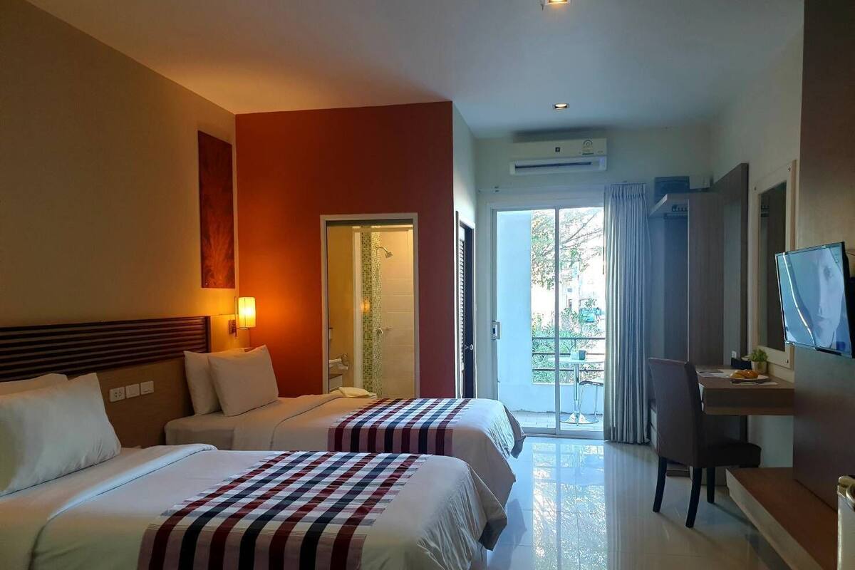 A hotel room with two beds, a desk, a TV, and a balcony with a view.