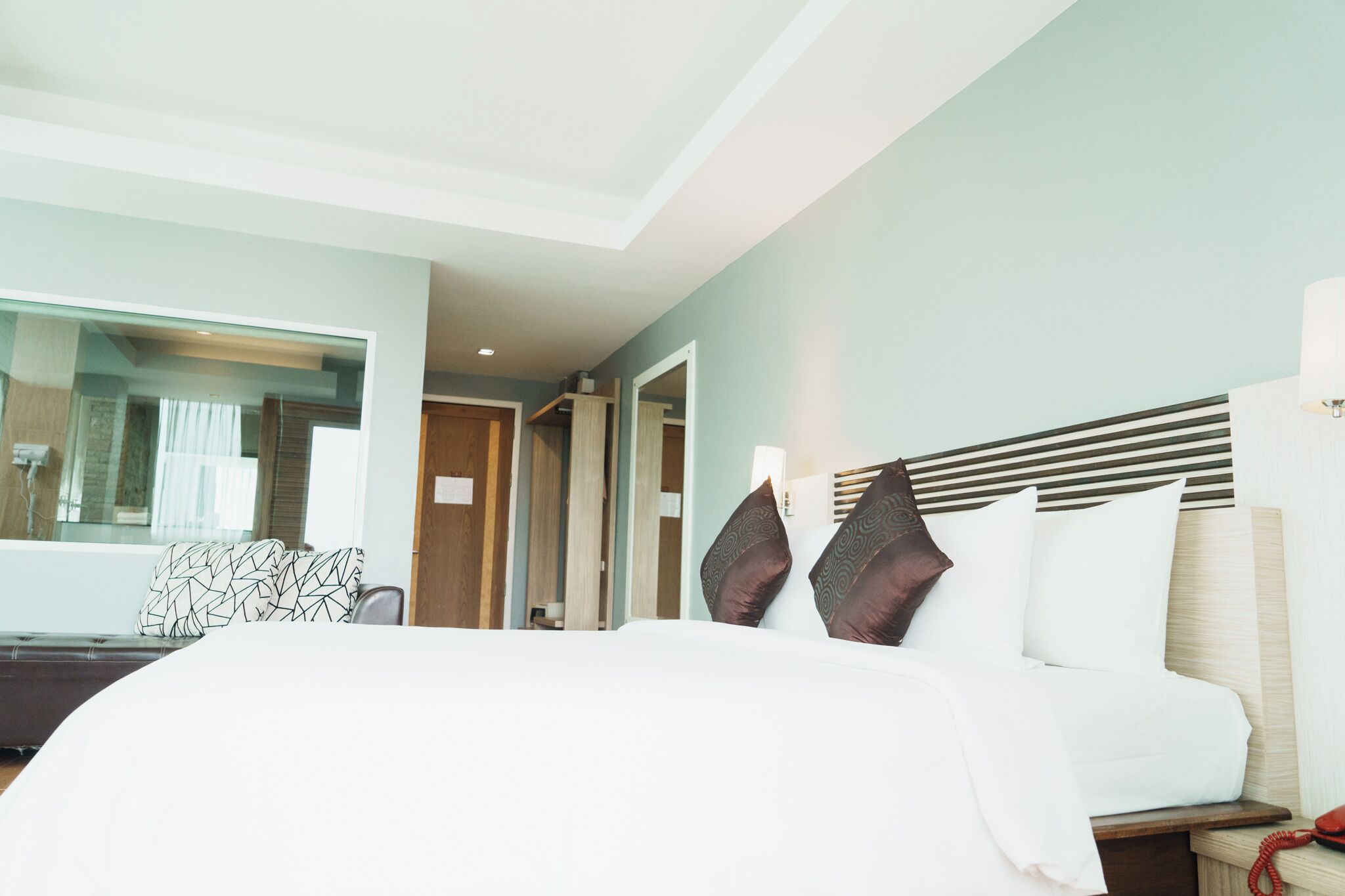 Ein Hotelzimmer mit Bett, Nachttisch, Spiegel und Blick auf den Flur.