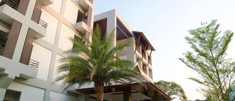 Un hotel de varios pisos con balcones, una entrada cubierta y vegetación circundante.