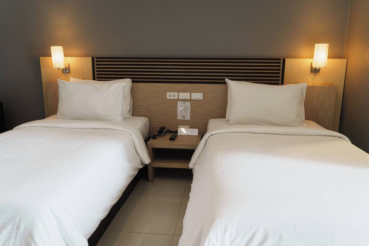 A hotel room with two single beds, a wooden headboard, bedside lamps, a phone, and a small table.