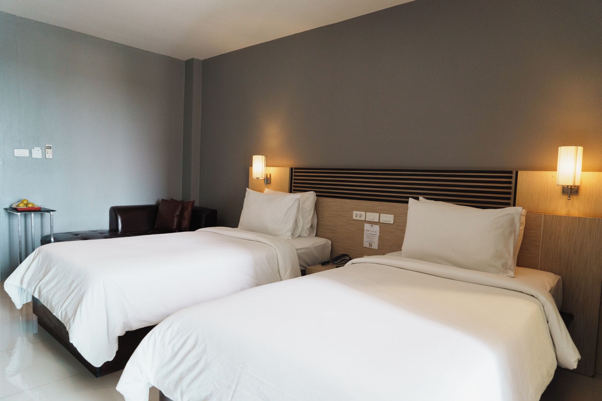 Een hotelkamer met twee bedden, een kleine tafel met een schaal fruit en wandlampen.