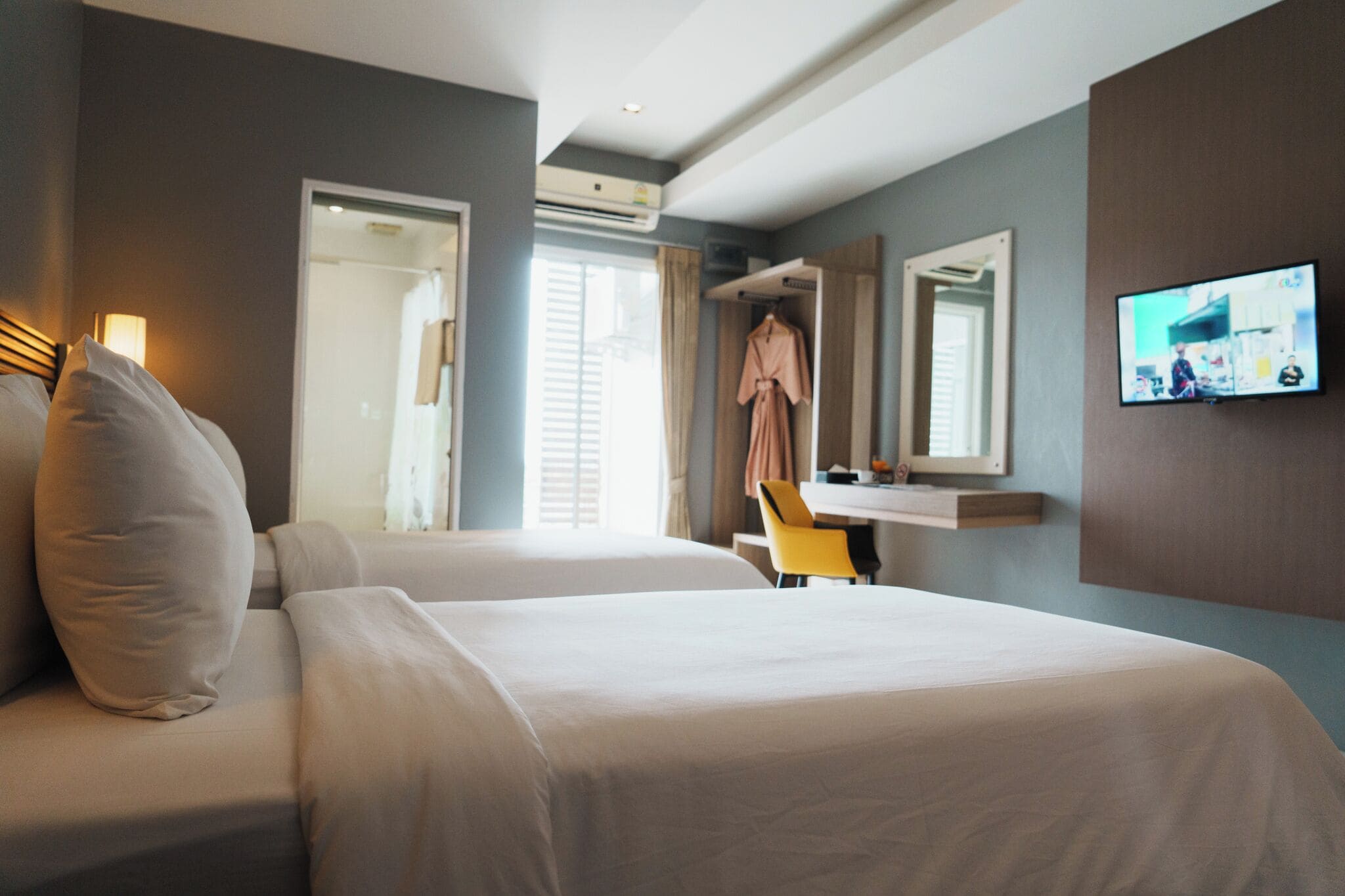 Habitación de hotel con dos camas, un escritorio, una silla, un televisor y una bata colgada en la pared.