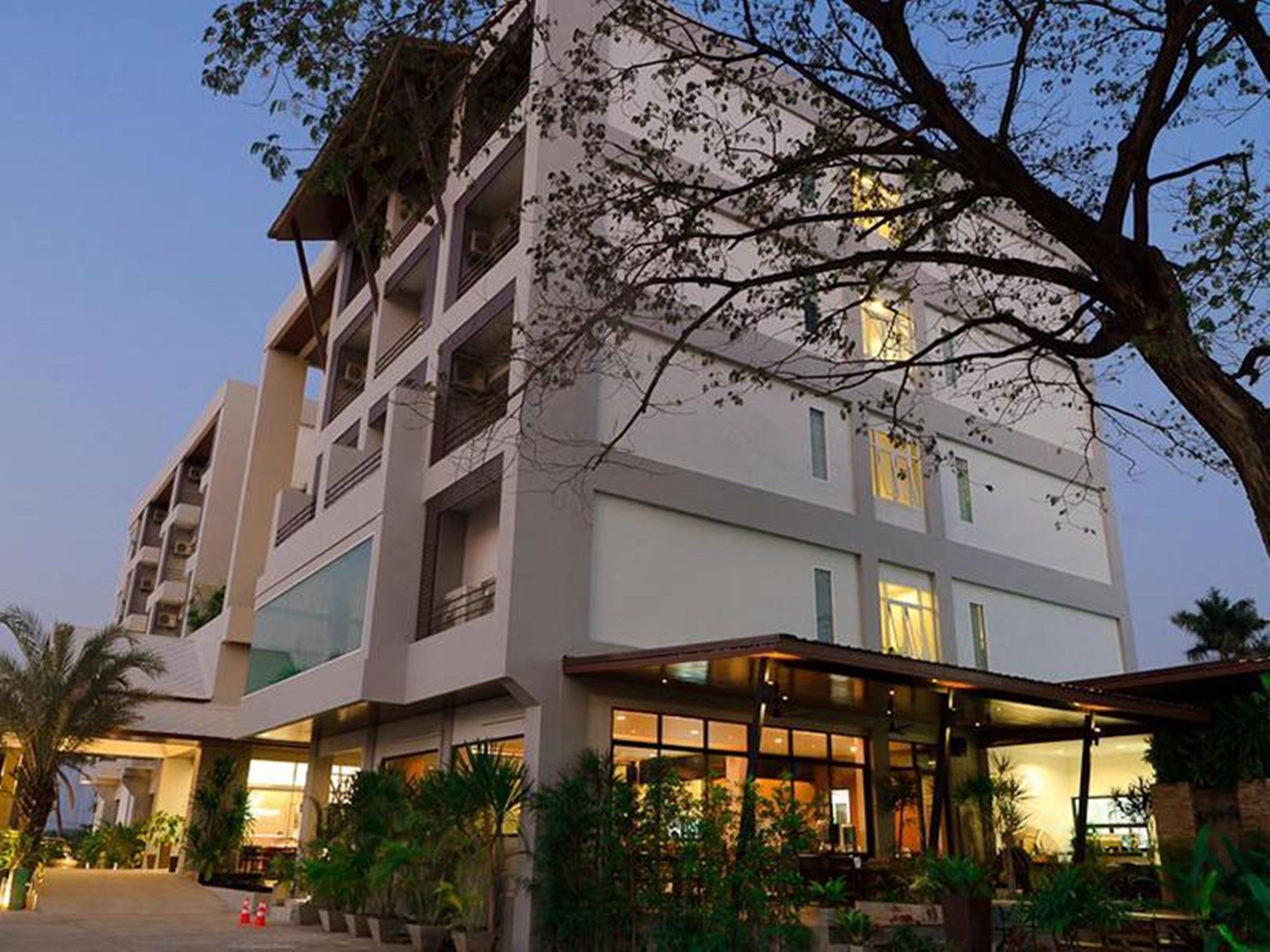Un hôtel à plusieurs étages au design moderne, doté de balcons, de grandes fenêtres et d’un hall d’entrée bien éclairé avec des espaces de détente en plein air.
