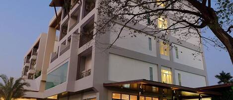 A multi-story hotel with a modern design, featuring balconies, large windows, and a well-lit entrance area with outdoor seating.