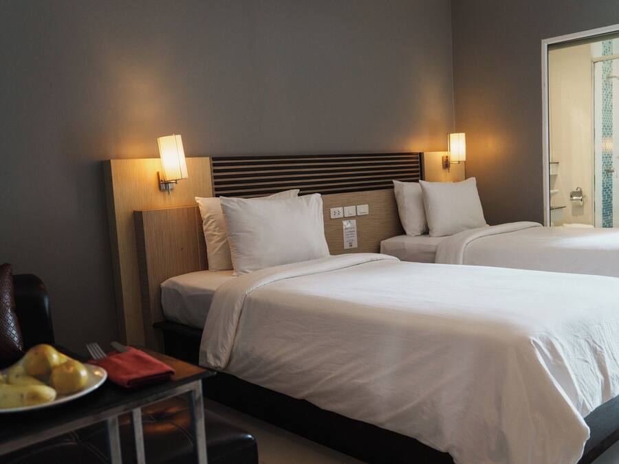 Une chambre d’hôtel avec deux lits, une table de chevet sur laquelle se trouve une assiette de fruits et des lampes fixées au mur.
