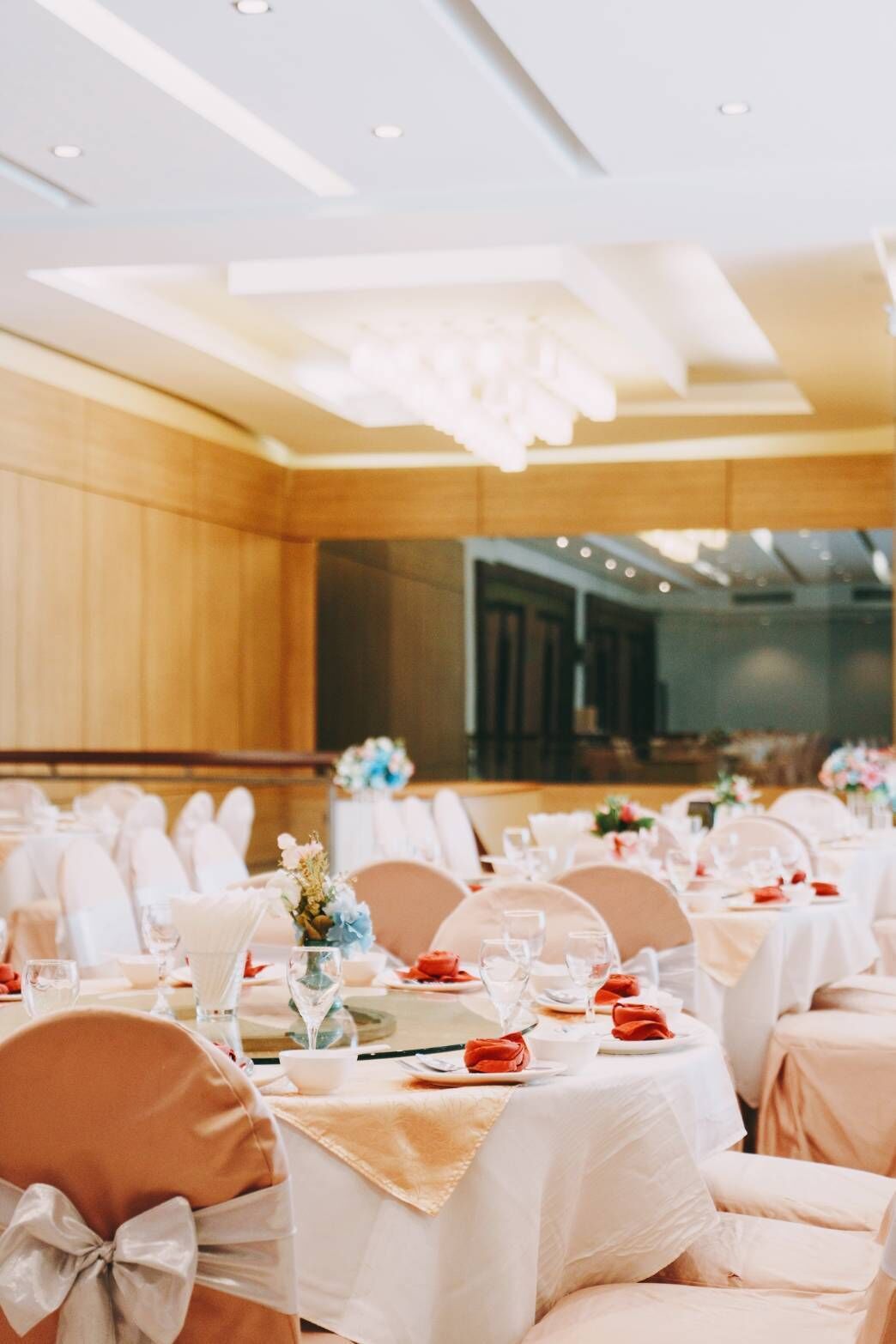 A banquet hall with round tables set for a formal event, featuring white tablecloths, red napkins, and floral centerpieces.