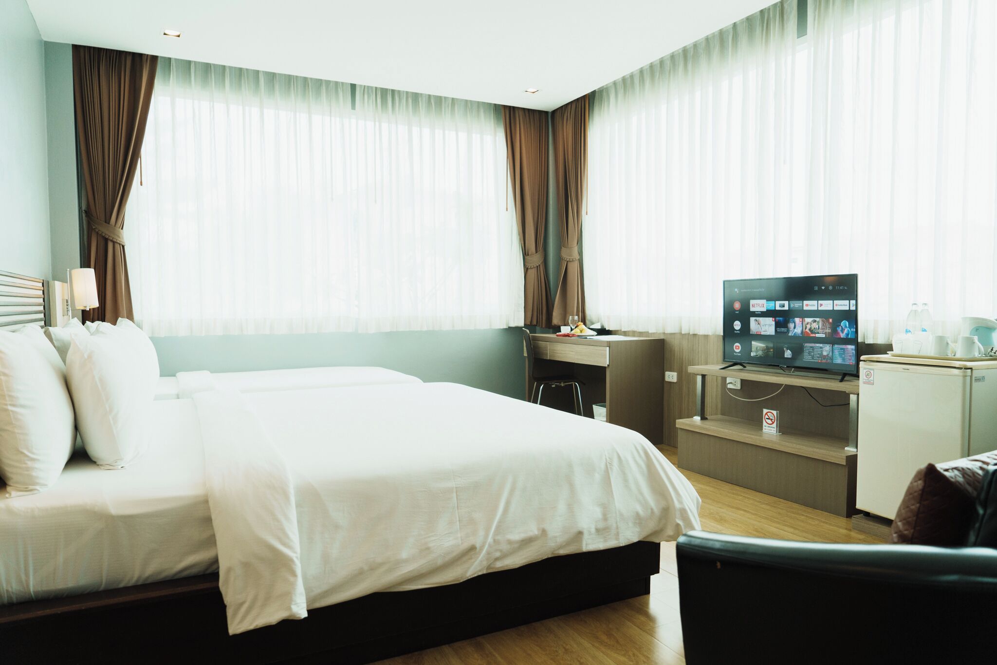 Hotellihuone, jossa on suuri sänky, työpöytä tietokoneella, televisio ja minibaari.