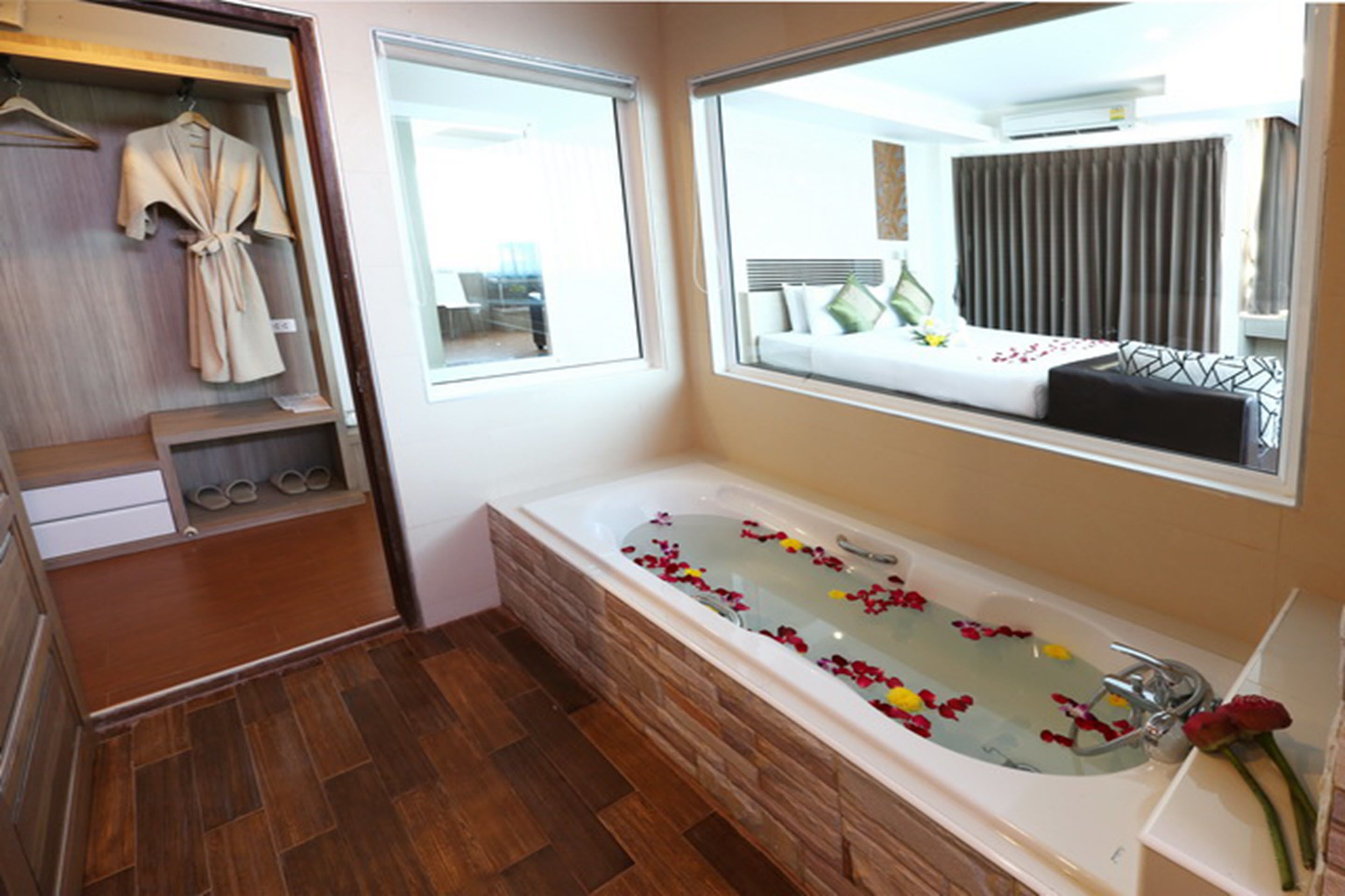 A bathroom with a large bathtub, wooden flooring, a mirror, and a window.