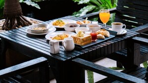 A table set with breakfast items and a glass of orange juice, surrounded by lush greenery and a small pond. - Green Hotel & Resort Khon Kaen (Khon Kaen)