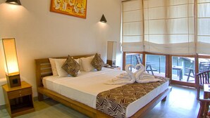 A spacious bedroom with a large bed, wooden ceiling beams, an air conditioning unit, a wall-mounted artwork, and a view of the outside through large windows. - Elephant Trail (Udawalawa)