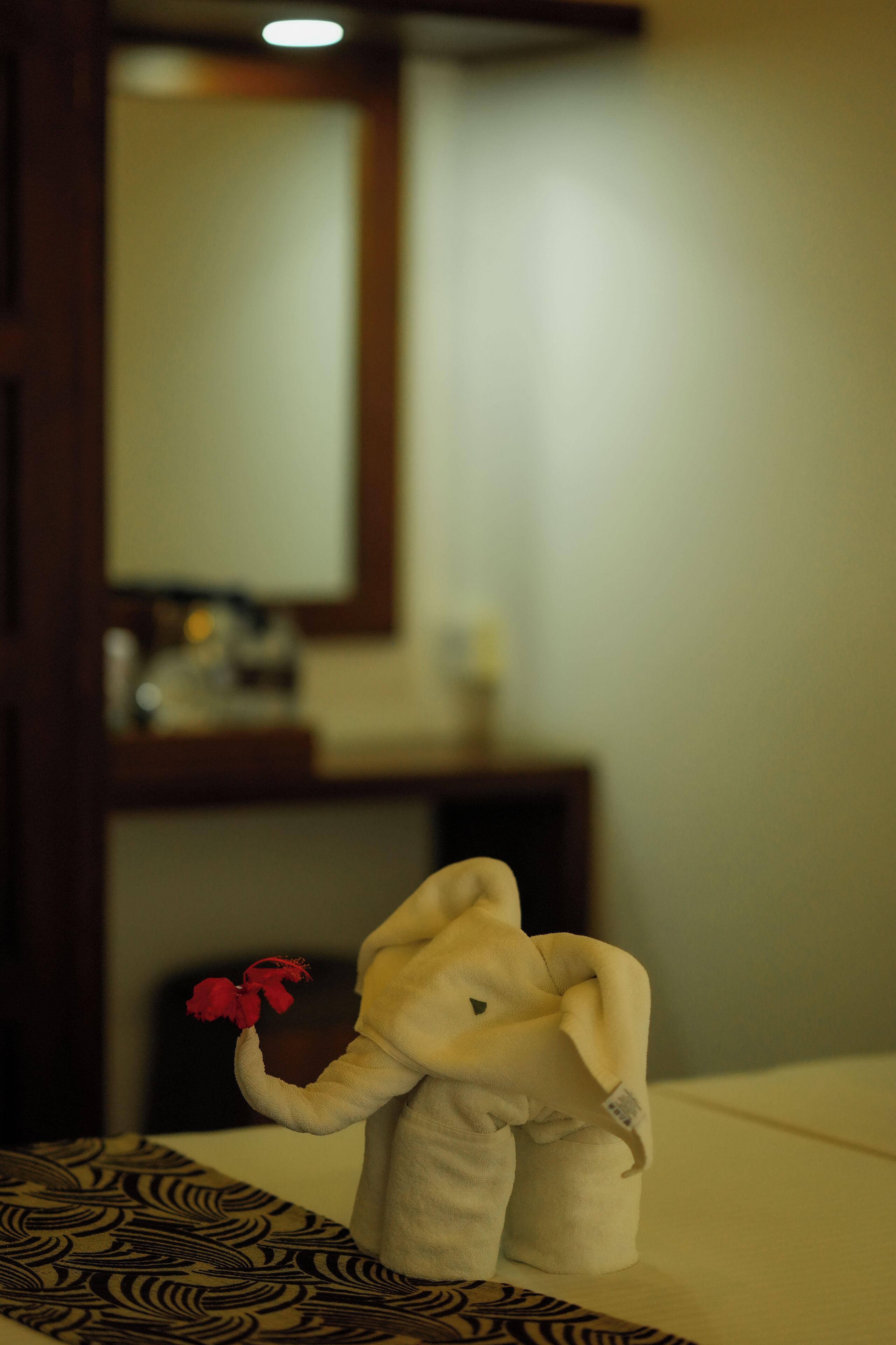 Un coussin moelleux en forme d’éléphant, orné d’une fleur rouge, est posé sur un lit.