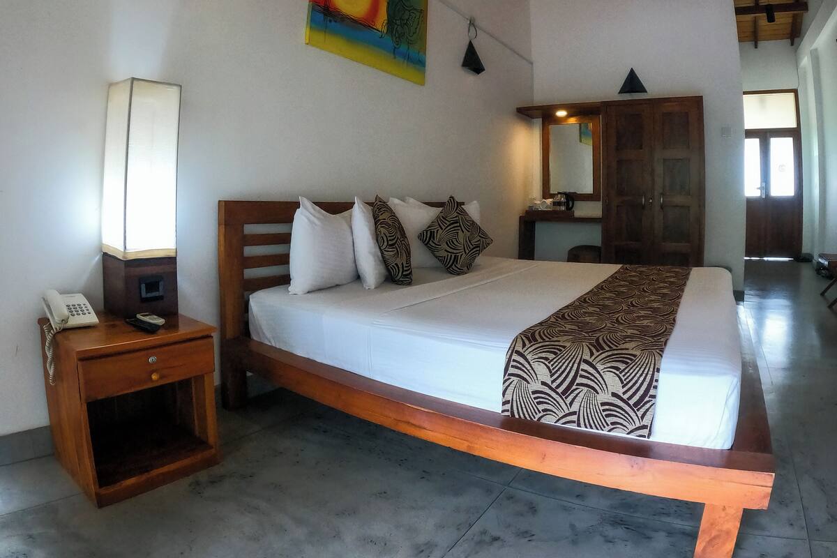 A bedroom with a bed, bedside table, lamp, and a painting on the wall.