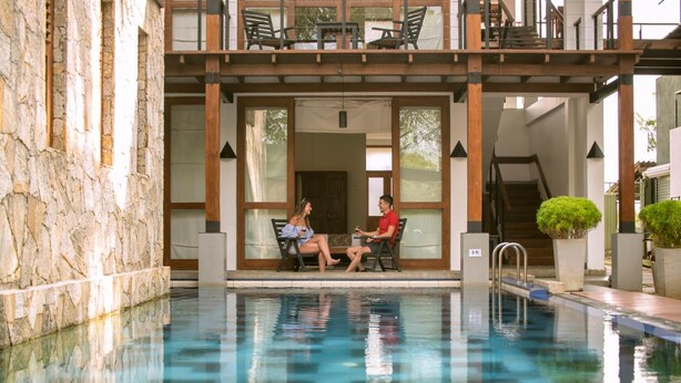 A pool area with a stone wall, a wooden deck with chairs, and a staircase leading to an upper level. - Elephant Trail (Udawalawa)