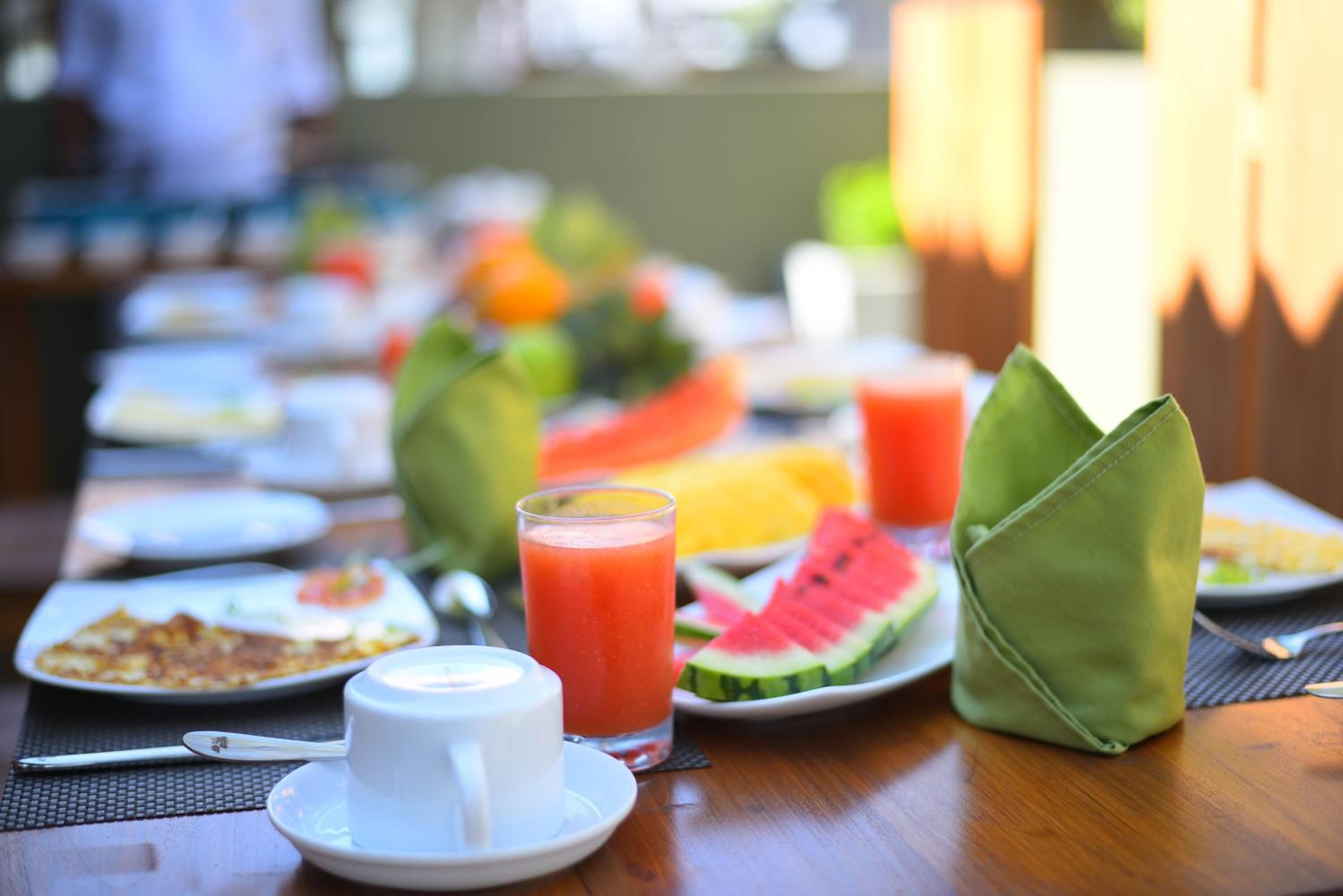 Une table mise pour le petit-déjeuner, avec des assiettes remplies de nourriture, un verre de jus de fruits et un porte-serviettes vert.