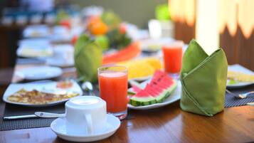 Une table mise pour le petit-déjeuner, avec des assiettes remplies de nourriture, un verre de jus de fruits et un porte-serviettes vert.