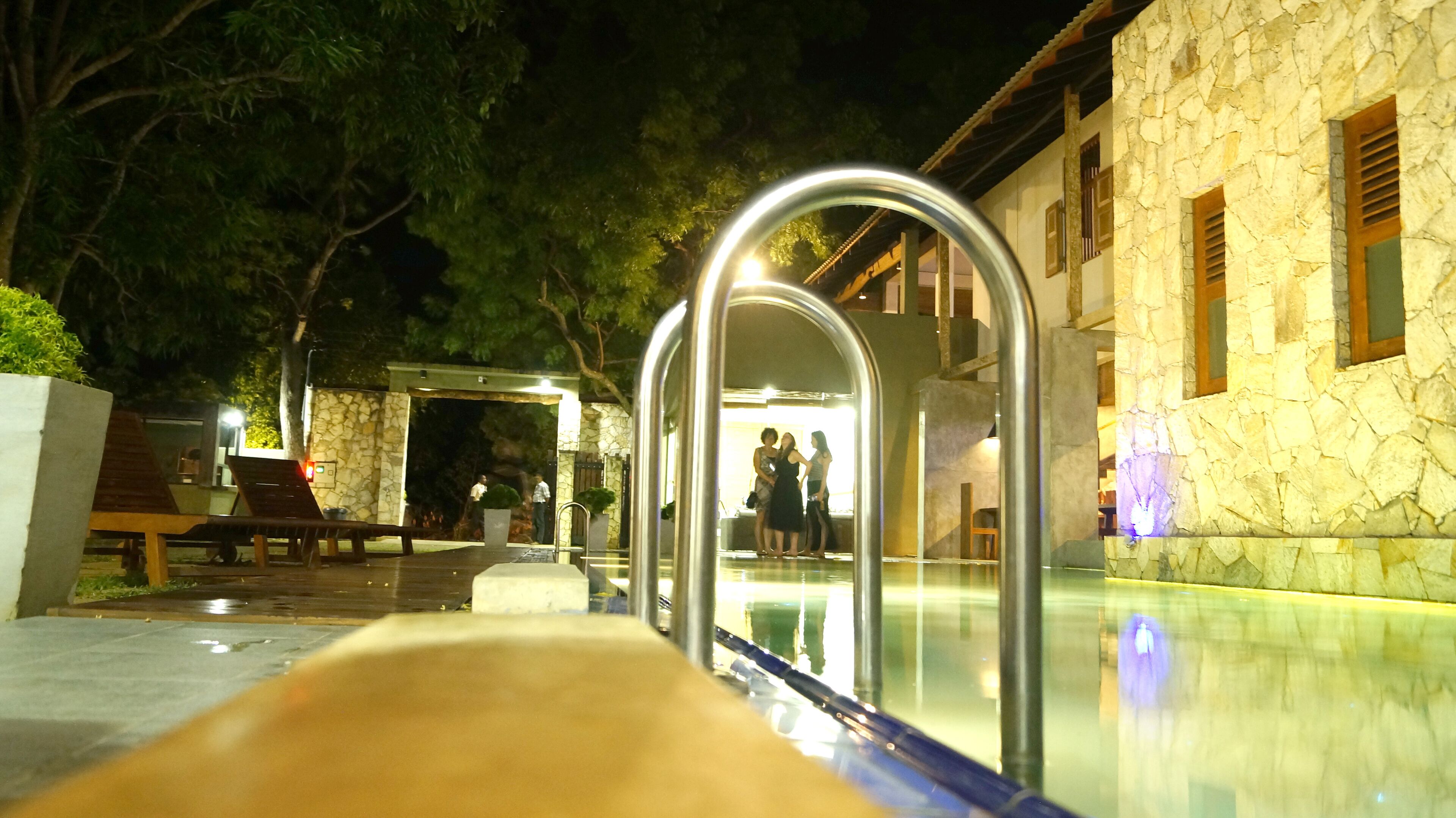 Un área de piscina con un muro de piedra y un arco de metal que da a un edificio.