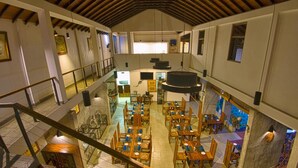A spacious restaurant with multiple dining tables and chairs, a mezzanine level, and a high ceiling with exposed beams. - Elephant Trail (Udawalawa)
