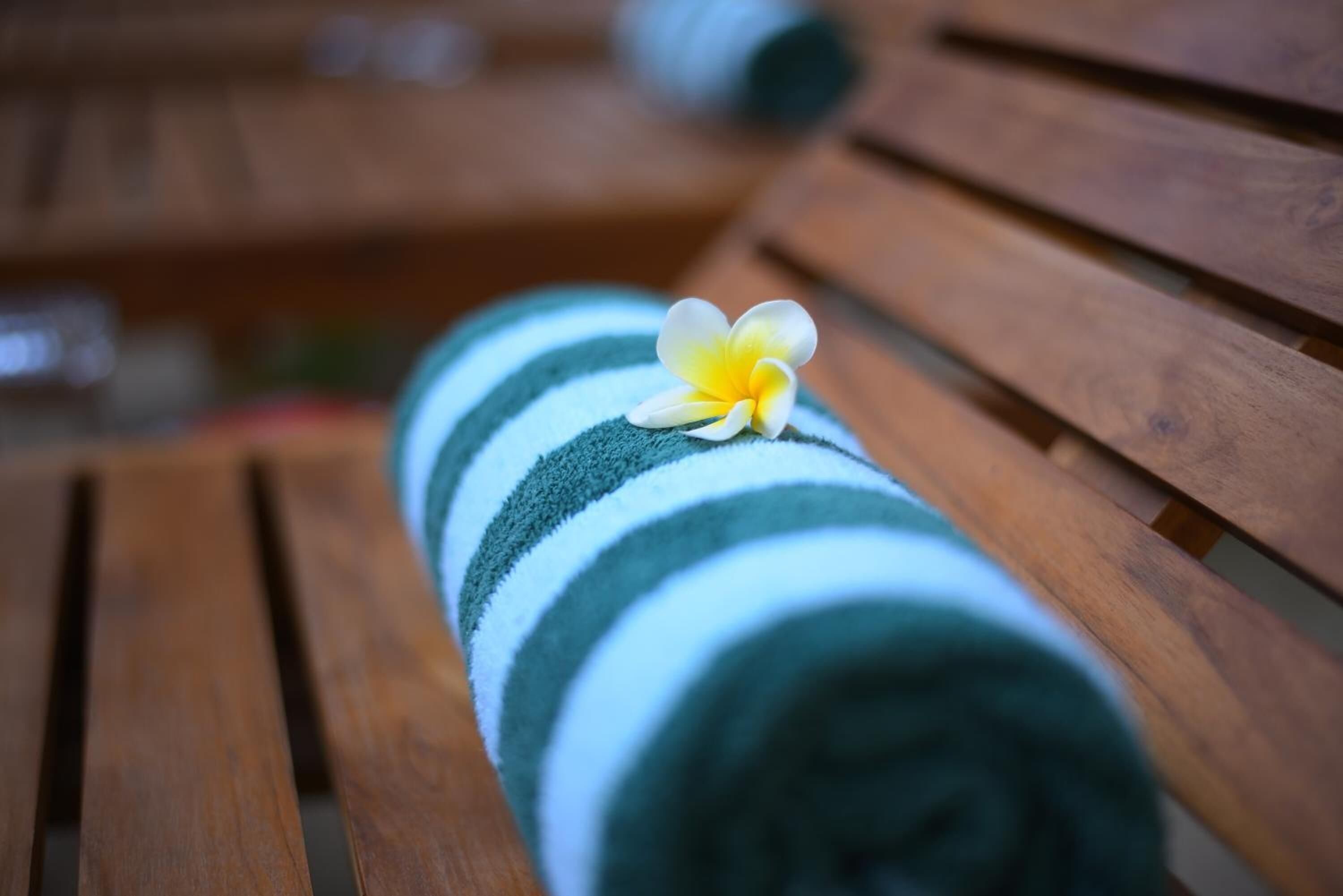 A rolled towel with a yellow flower on a wooden bench.