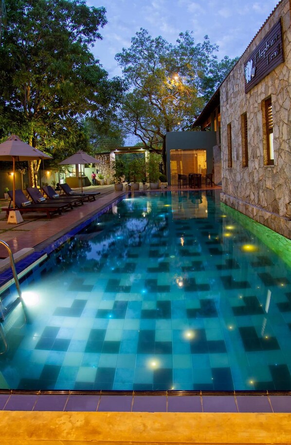 A swimming pool with lounge chairs and umbrellas, surrounded by stone walls and trees.