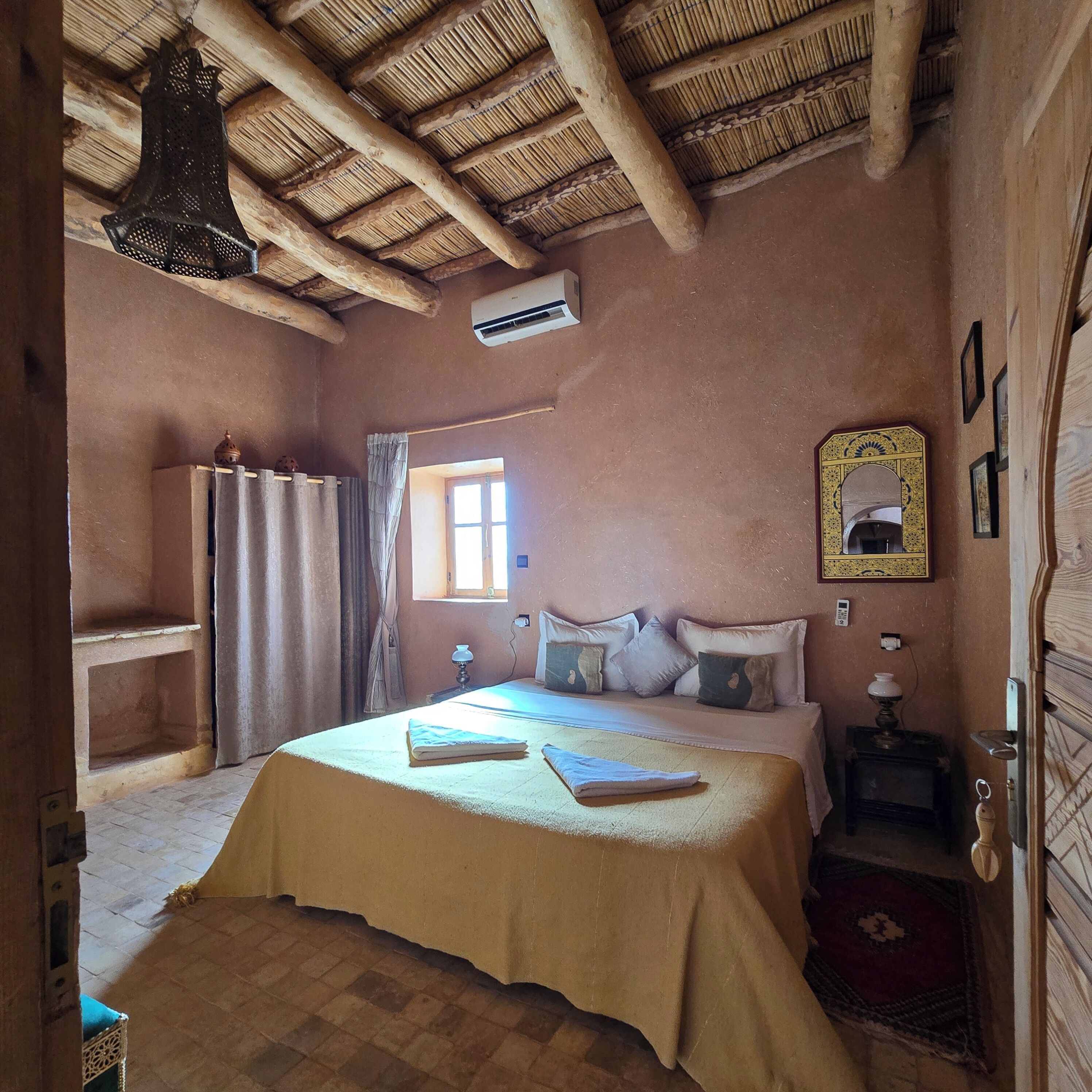 A room with a bed, a window, a mirror, and a door.